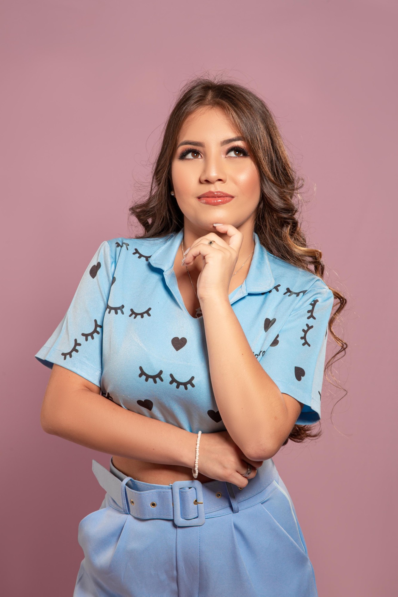 Raissa Carolina de blusa azul com cílios estampados, com a mão no queixo